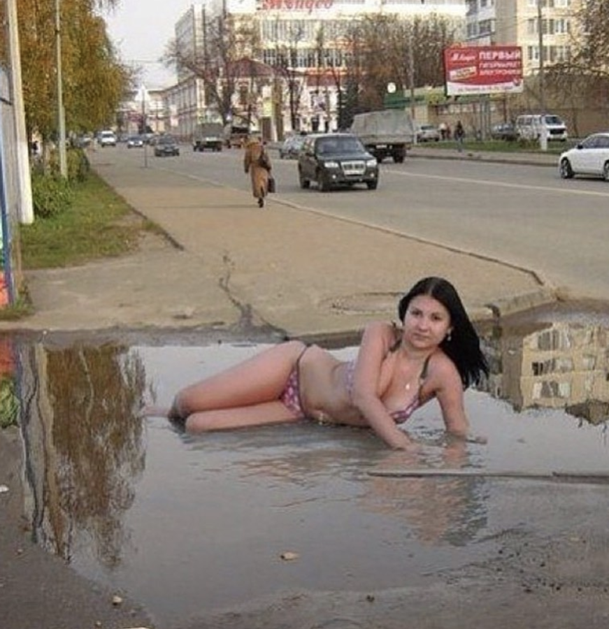 woman in her bikini, posing in a puddle of dirty rain water accumlated on the side of the road